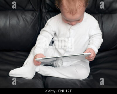 Bébé garçon âgé d'un an dans un livre blanc à sleepsuit a tablet computer Banque D'Images