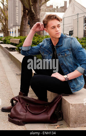 Young Caucasian man en veste en jean et jean noir assis sur un mur à Londres Banque D'Images