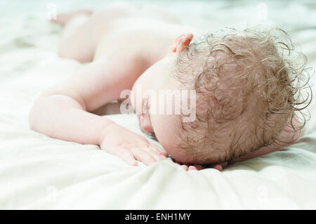 Curly haired Woman bébé garçon endormi sur le lit avec les cheveux mouillés après le bain Banque D'Images