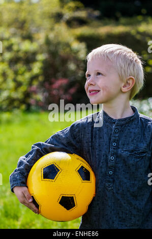 Enfant d'âge préscolaire avec le football, ballon de football. Boy c'est dans le jardin avec son football . Son football est jaune. Il porte un Banque D'Images