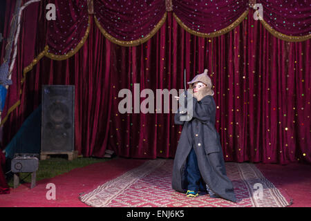 Young Boy Wearing Clown composent, Hat et plus grand manteau et tenant un sabre sur scène avec rideau rouge Banque D'Images