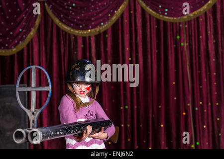 Dur à la fille avec visage peint sur le port casque de taille moyenne tenant les grandes Armes à canon double sur scène avec rideau rouge Banque D'Images