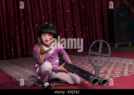 Girl Wearing Helmet Combat accroupi sur sol avec Grand Lit Double Barrelled shot gun avec fer Vue sur scène avec rideau rouge Banque D'Images