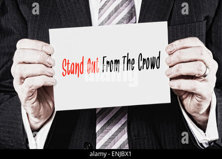Un homme tenant une carte d'affaires avec les mots, de se démarquer de la foule, écrit dessus. Banque D'Images
