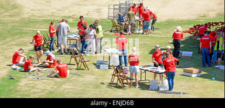 Des bénévoles de coquelicot travaillent à la Tour de Londres douve sec chaud jour d'été assemblage de coquelicots en céramique rouge à tiges de fil sang balayées terres et Mers Angleterre Royaume-Uni Banque D'Images