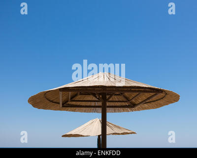 Parties supérieures de deux parasols en paille contre le ciel bleu et la mer. Banque D'Images