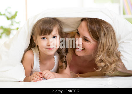 Heureux l'enfant et sa mère allongé sous couverture dans le même lit Banque D'Images