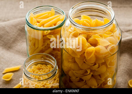 Différents types de pâtes macaronis jaune dans bol en verre sur fond de tissu tissu jute Banque D'Images