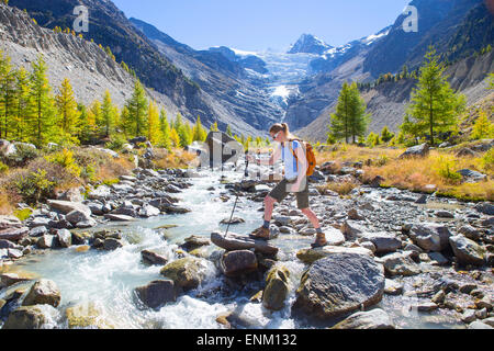 Un female hiker est traversée d'un cours d'eau des glaciers dans les Alpes suisses. Banque D'Images