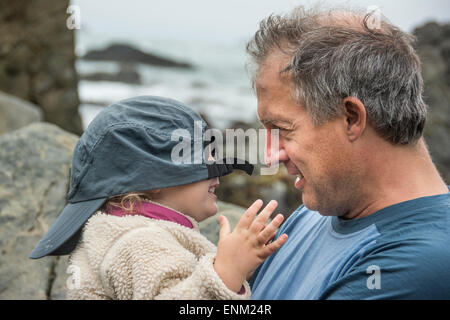 Père joue à cache-cache avec l'aide de sa fille bébé baseball cap chez Patrick Point State Park, Californie. Banque D'Images