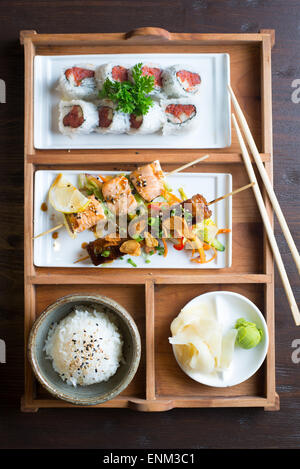 Un assortiment d'aliments de style japonais dans une 'boîte bento" plateau en bois avec des baguettes Banque D'Images