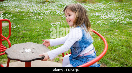 Petite fille se transforme en un carrousel manuel dans une aire de jeux extérieure Banque D'Images