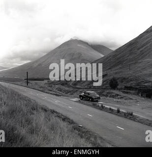 Années 1950, historique, une couverture de nuages couvre les sommets de montagne et les vallées environnantes de la région de Lochaber dans les Highlands écossais, avec une voiture de l'époque garée dans un laprès de la piste sinueuse du chemin de fer du pont Spean. Le Monument Commando, qui commémore les commandos qui ont été entraînés dans la région entre 1942 et 1945, est à proximité. Banque D'Images