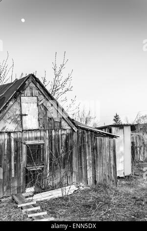 Lune qui brille au-dessus d'un village rustique en bois hangar avec des toilettes extérieures et la lune dans un ciel sans nuages Banque D'Images