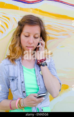 Girl talking on l'un téléphone pendant la lecture d'un message texte sur un fond coloré Banque D'Images