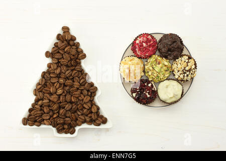 Les grains de café torréfié en blanc lave-spruce, ensemble de chocolats dans la soucoupe ronde blanche sur le fond en bois blanc Banque D'Images