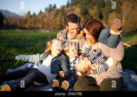 Une famille de cinq personnes rire ensemble tout en étant assis sur une couverture. Banque D'Images