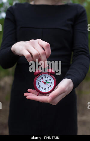 Les femmes en robe noire holding red réveil par une part Banque D'Images