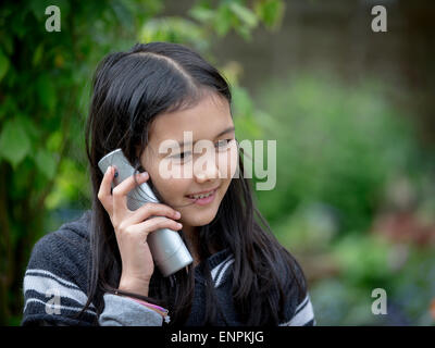 Portrait of a happy 9 ans thaï, l'anglais girl talking on un téléphone dans un jardin Banque D'Images