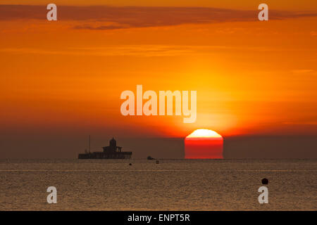 Herne Bay, Kent, UK. 10 Mai 2015 : Météo France. Un matin brumeux le ciel donne une lueur rouge-orange au lever du soleil sur les ruines de Herne Bay pier, qui a été endommagé par les tempêtes dans les années 1970, et la section centrale avait démantelé. Un bateau de pêche à la ligne est vu partir pour un voyage de pêche tôt le matin. La température peut atteindre jusqu'au début des années 20 le lundi Banque D'Images