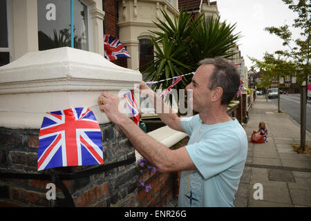 Un homme est suspendu à l'extérieur de l'Union jack drapeaux une maison pendant une partie de la rue pour célébrer le 70e anniversaire du Jour de la victoire à Portsmouth, Royaume-Uni. Banque D'Images