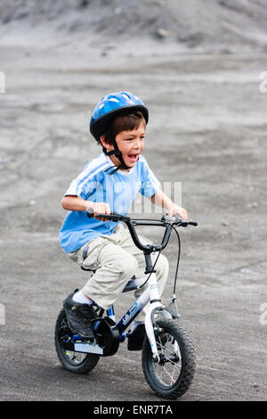 Enfant, garçon, 9-10 ans, à vélo d'enfant sur un sol ouvert tout en portant un casque d'accident, et regardant très excitée et criant. Banque D'Images