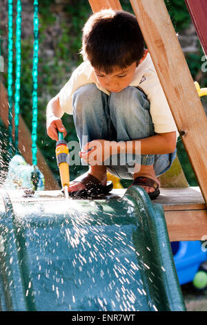 Young boy, huit ans. Vue avant, pas de contact avec les yeux, accroupi sur le jeu-cadre, tenue flexible, jaillit de l'eau, les éclaboussures Banque D'Images