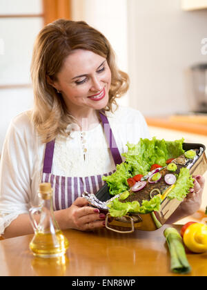 Cook - cute femme d'âge moyen dans la cuisine poissons grill Banque D'Images