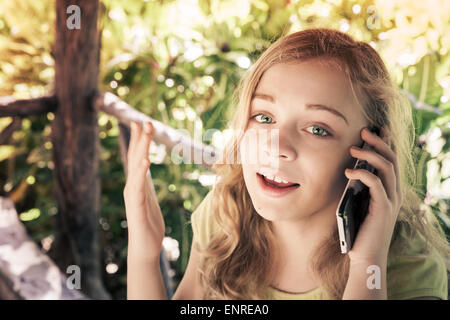 Portrait plein air de beau blond Caucasian teenage girl in a park parler sur un téléphone cellulaire, effet de filtre photo aux tons vintage Banque D'Images