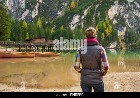 Une brunette woman randonneur, portant l'équipement de plein air est debout à la recherche à la vue du lac Bries. Bateaux en bois rustique, d'une jetée, et golden et arbres verts représentent l'automne. Banque D'Images