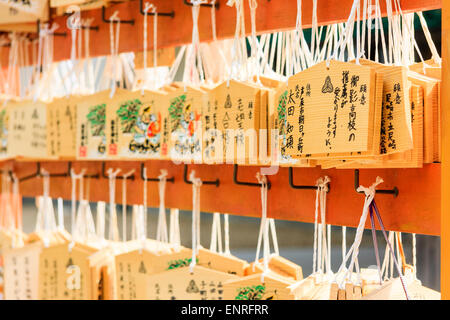 Tableaux ema japonais, tablettes de souhaits, suspendus à des cadres de travail par des cordes rouges dans un sanctuaire Shinto. Les espoirs, les souhaits et les dédicaces sont écrits sur eux. Banque D'Images