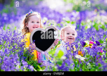 Enfants jouant dans la forêt jacinthes. Petite fille et petit garçon tenant une forme de coeur en bois tableau debout dans un parc Banque D'Images