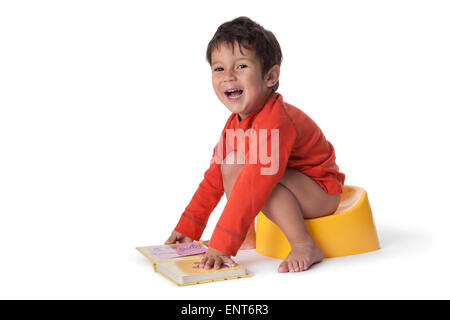 Bébé garçon assis sur un pot et avec un livre sur fond blanc Banque D'Images