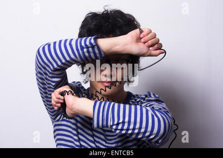 Asian young man looking through arms holding head phone chord Banque D'Images