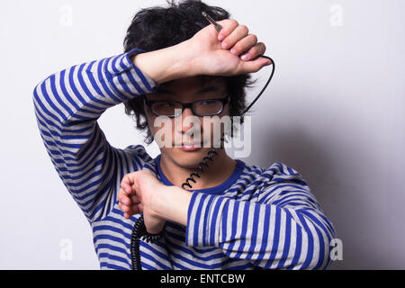 Asian young man looking through arms holding head phone chord Banque D'Images