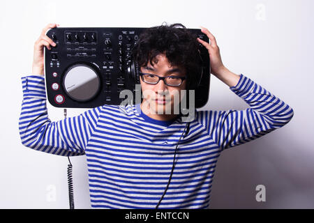 Jeune homme asiatique à la recherche de l'appareil photo numérique en tenant le tourne-wearing head phones Banque D'Images