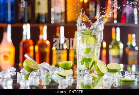 Mojito cocktail verre avec splash, servi sur comptoir bar avec des bouteilles sur fond flou Banque D'Images