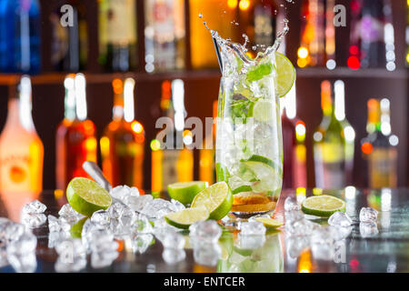 Mojito cocktail verre avec splash, servi sur comptoir bar avec des bouteilles sur fond flou Banque D'Images