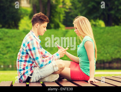Les smartphones avec couple sitting on bench in park Banque D'Images