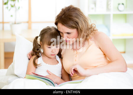 Mère et fille heureux enfant lire un livre au lit Banque D'Images