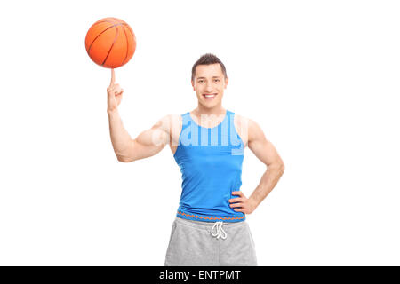 Young cheerful sportsman la rotation d'un terrain de basket-ball sur son doigt et regardant la caméra isolé sur fond blanc Banque D'Images