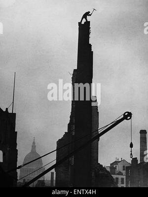 James Woods Workman démolir une cheminée avec sa pioche dans l'ombre de la cathédrale St Paul, après que le bâtiment a été endommagé au cours d'un raid aérien pendant la Seconde Guerre mondiale. Mars 1942. Banque D'Images