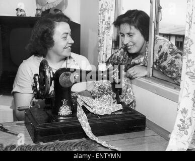 Occupé à sa machine à coudre est Mme Beaty Evans, sa voisine, Mme Betty Davies ressemble à la fenêtre pour discuter des derniers maillot. Juillet 1955 Banque D'Images