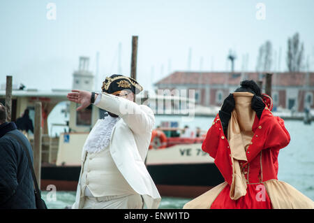 Deux artistes de rue, hommes et femmes, déguisés en personnages de commedia dell'arte se cachant de la caméra sur une rue à Venise Banque D'Images