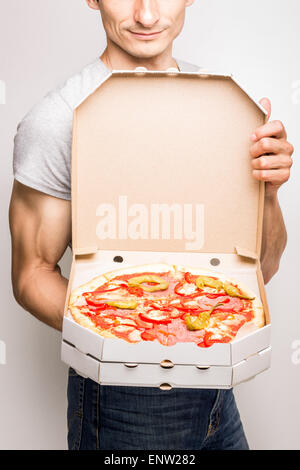 Jeune homme propose un emballage ouvert avec pizza savoureuse tenant dans ses mains Banque D'Images