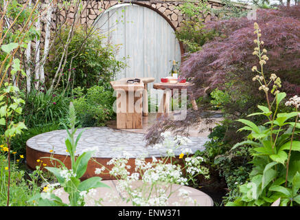 Cottage jardin de campagne petit cercle circulaire patio avec porte de lune ronde - table en bois et banc acer palmatum arbre et frontières mixtes Royaume-Uni Banque D'Images