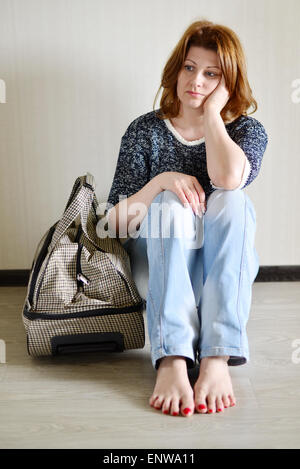 Femme triste assis près du mur avec une valise parce qu'un divorce Banque D'Images
