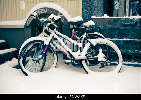 Deux vélos de montagne laissés dans la neige, appuyé contre un mur. Banque D'Images