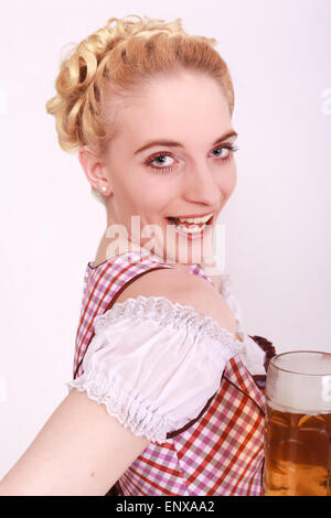 Vue de côté avec regarder dans l'appareil photo d'une jeune femme dans la dirndl avec une verseuse en verre de bière plein Banque D'Images