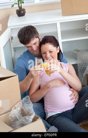 Cheerful couple célébrant la grossesse et dépose avec champagne assis sur le plancher Banque D'Images